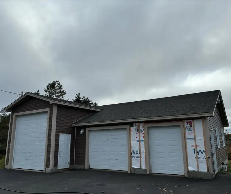 Triple-bay garage with a new dark shingled roof under a grey sky