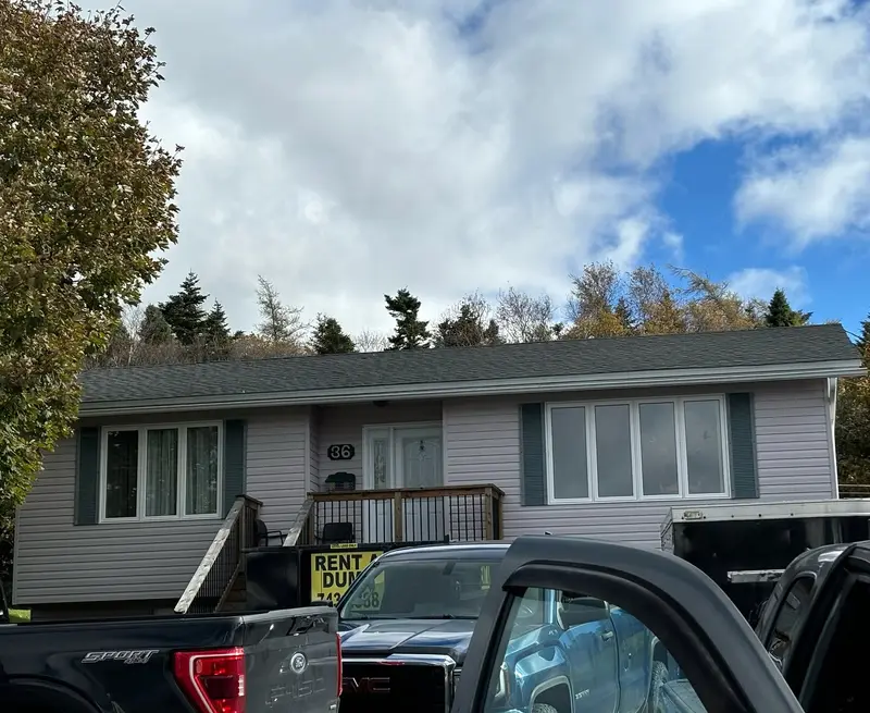 Split-entry house with a grey roof, a waste bin and a truck in the foreground