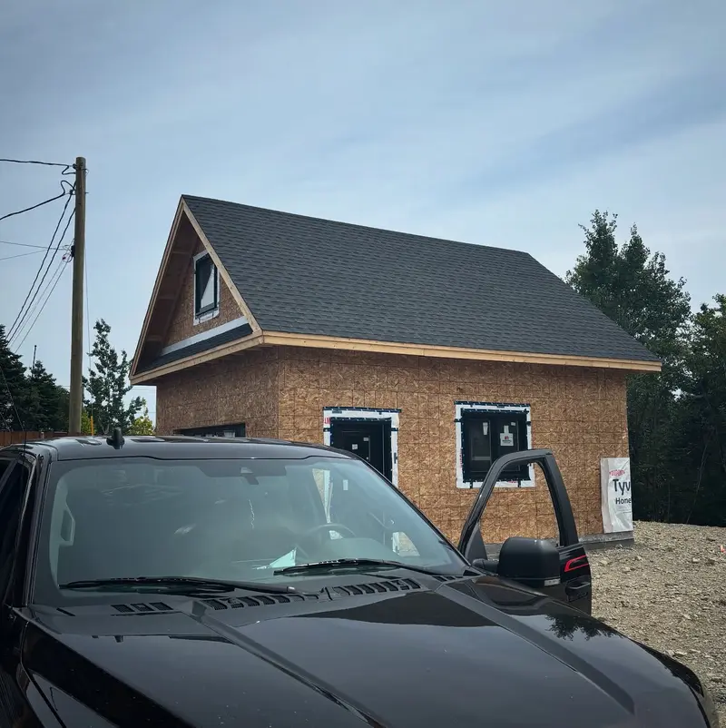 Newly built garage with a dark shingled roof and a pickup truck in front