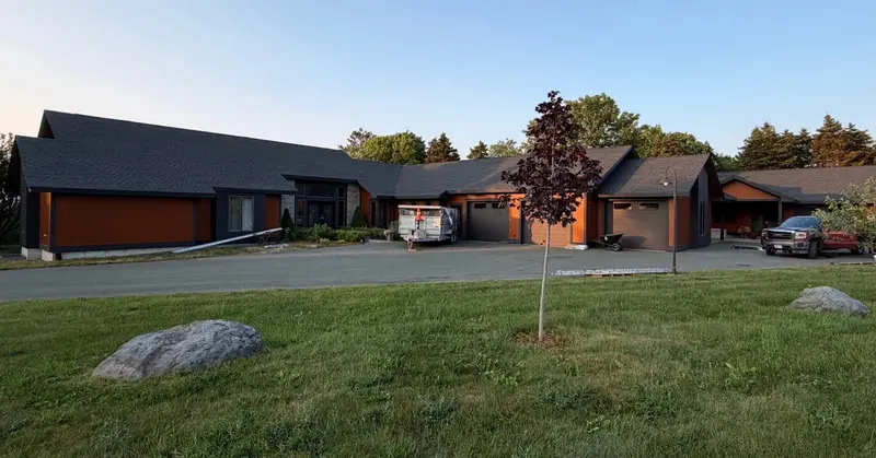 Long modern bungalow with a dark shingled roof across a wide lawn